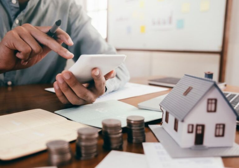 person-using-a-calculator-with-a-stack-of-coins-and-house-figurine-in-front-of-them-768x542.png