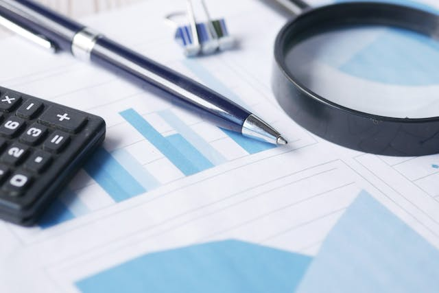 a-calculator-magnifying-glass-and-a-pen-on-a-bunch-of-graphs.png