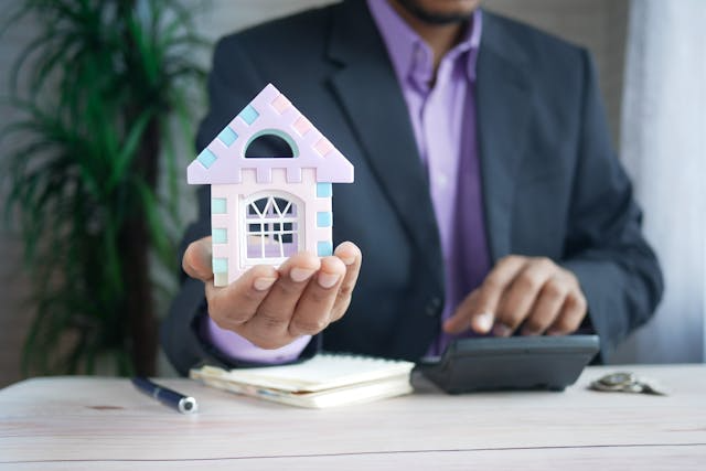 a-person-holding-a-home-figurine-and-putting-numbers-into-a-calculator.png