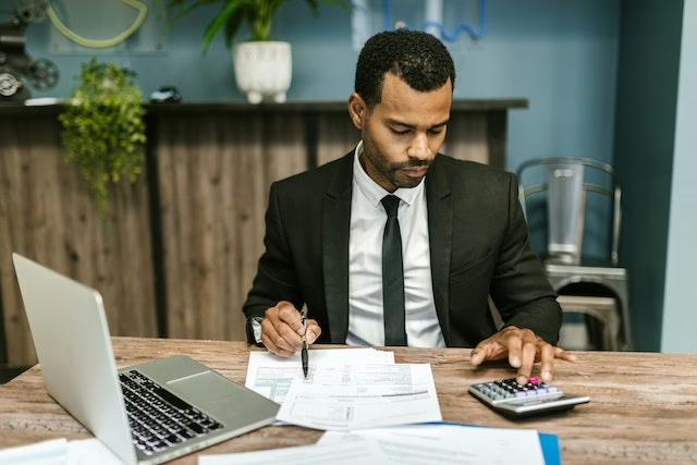 finance-expert-looking-over-documents-and-confirming-calculations-on-a-calculator.png