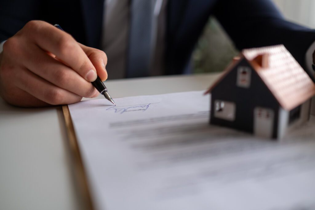 a-person-signing-a-document-with-a-house-figurine-one-it-1024x683.png