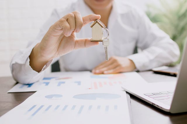 a-person-holding-a-house-figurine-and-key-with-documents-around-them.png