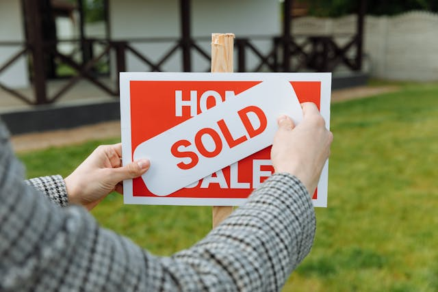 a-real-estate-agent-placing-a-sold-sticker-over-a-for-sale-sign.png